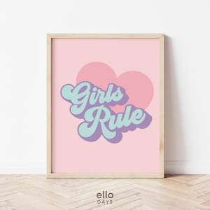 May include: A pink and white printable wall art print with a heart shape and the text "Girls Rule" in a retro font.