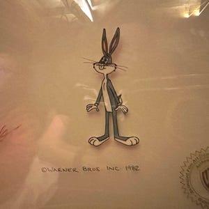Puede incluir: Un celuloide de dibujos animados de Bugs Bunny de Warner Bros. Inc. 1982. La imagen presenta a Bugs Bunny en su pose clásica, con una combinación de colores gris y blanco. El celuloide está firmado e incluye el logotipo de Warner Bros.