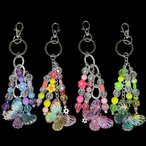 Puede incluir: Cuatro llaveros con colgantes de mariposa. Cada llavero presenta un cierre plateado, cuentas claras y coloridas y un dije de mariposa brillante. Los llaveros tienen una variedad de colores, incluyendo rosa, amarillo, verde y morado.