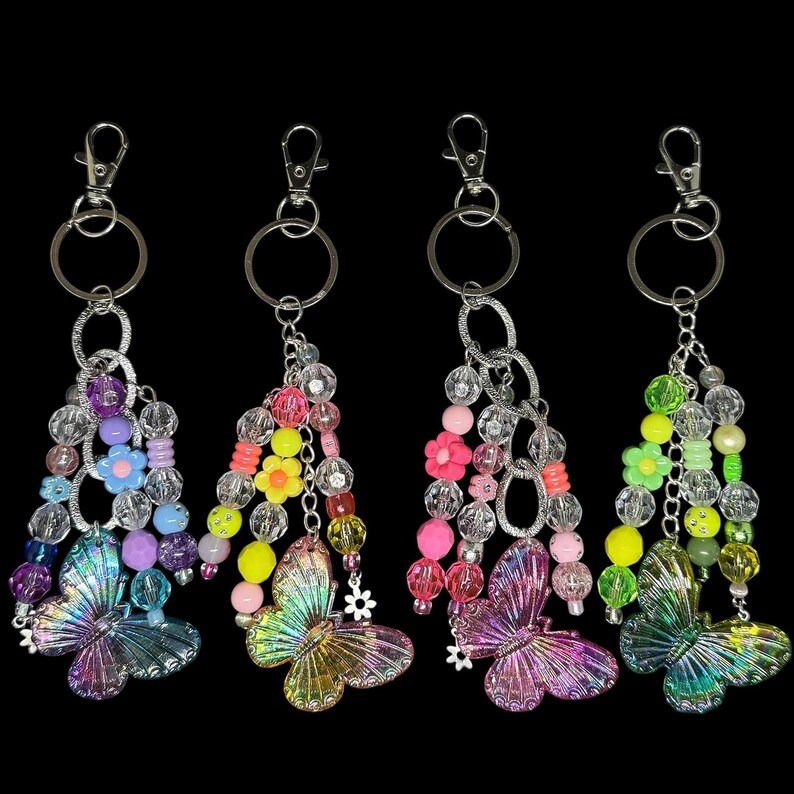 Puede incluir: Cuatro llaveros con colgantes de mariposa. Cada llavero presenta un cierre plateado, cuentas claras y coloridas y un dije de mariposa brillante. Los llaveros tienen una variedad de colores, incluyendo rosa, amarillo, verde y morado.