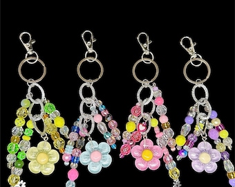 Könnte beinhalten: Vier Schlüsselanhänger mit Perlen, silberfarbenen Beschlägen und Blumenanhängern. Jeder Schlüsselanhänger hat ein anderes Farbschema aus Perlen, darunter Gelb, Grün, Rosa, Blau und Lila. Die Blumenanhänger sind farblich passend.