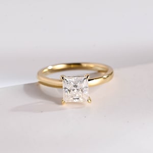 May include: A gold ring with a square-shaped clear gemstone.