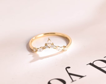 Puede incluir: Un anillo de oro con un diseño delicado y curvo adornado con pequeñas piedras preciosas transparentes. El anillo está sobre un fondo blanco.