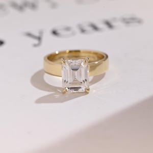 May include: A gold engagement ring with a large, clear emerald-cut diamond.
