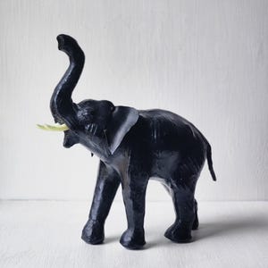 May include: A black elephant figurine with a raised trunk and ivory-colored tusks. The handcrafted sculpture has large ears and is posed on four legs. The elephant is a decorative item.