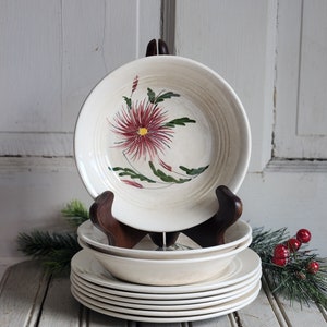 May include: A stack of white ceramic bowls with a floral design. The bowls have a red and green floral pattern with a yellow center. The bowls are stacked on a wooden stand.