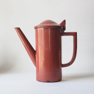 May include: A red enamel teapot with a hinged lid and a spout. The teapot has a simple, classic design.