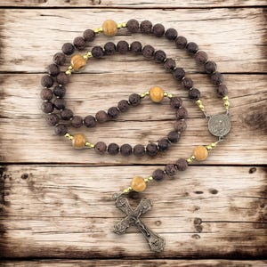 May include: A brown and gold rosary with wooden beads and a metal crucifix. The rosary is laid out on a wooden surface.