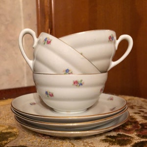 Può includere: Un set di tre tazze da tè e piattini in porcellana bianca con un motivo floreale. Le tazze hanno un bordo dorato e i piattini hanno una fascia dorata attorno al bordo.