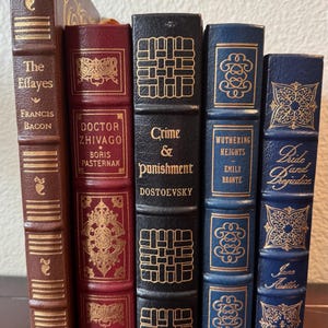 Może przedstawiać: Kolekcja klasycznych książek z dekoracyjnymi okładkami. Tytuły to "The Essays", "Doctor Zhivago", "Crime & Punishment", "Wuthering Heights" i "Pride and Prejudice". Książki mają złote litery i ozdobne wzory na grzbietach.