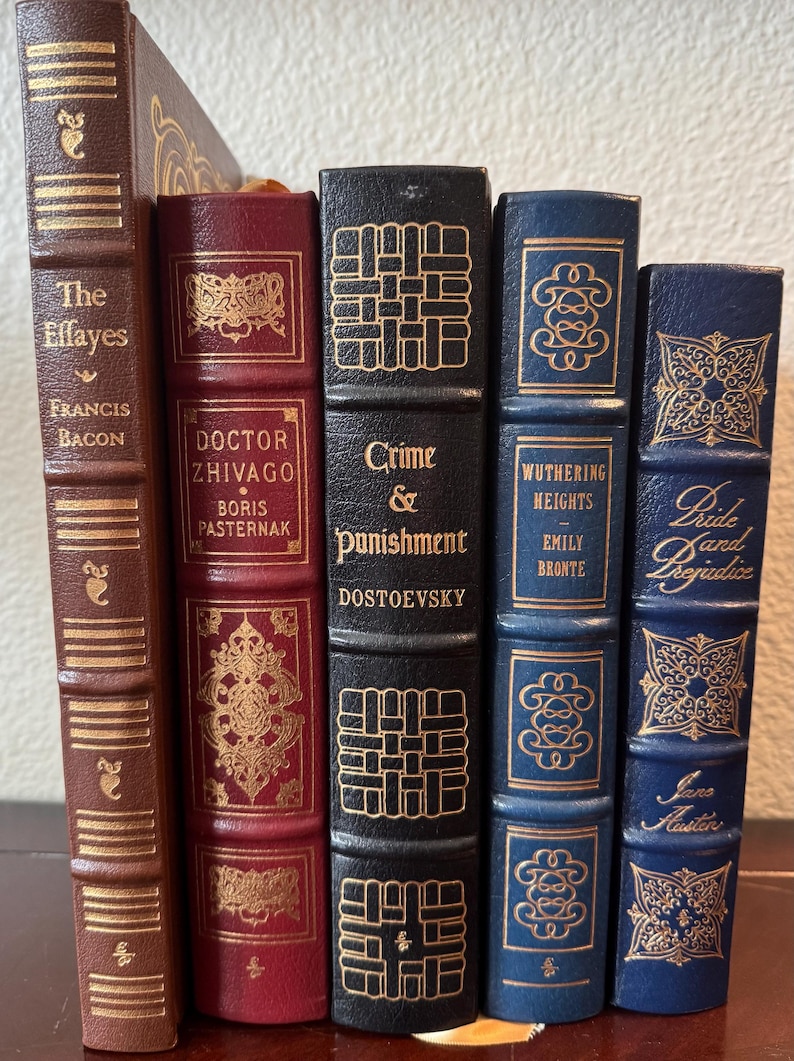 Może przedstawiać: Kolekcja klasycznych książek z dekoracyjnymi okładkami. Tytuły to "The Essays", "Doctor Zhivago", "Crime & Punishment", "Wuthering Heights" i "Pride and Prejudice". Książki mają złote litery i ozdobne wzory na grzbietach.