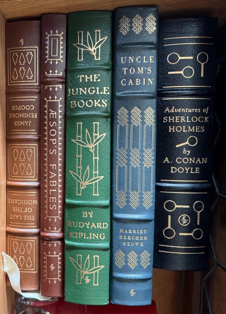 Może przedstawiać: Biały ceramiczny kubek z czarnym uchwytem i napisem "But First, Coffee" czarną, pogrubioną czcionką. Kubek stoi na drewnianej powierzchni. Kubek ma około 10 cm wysokości.