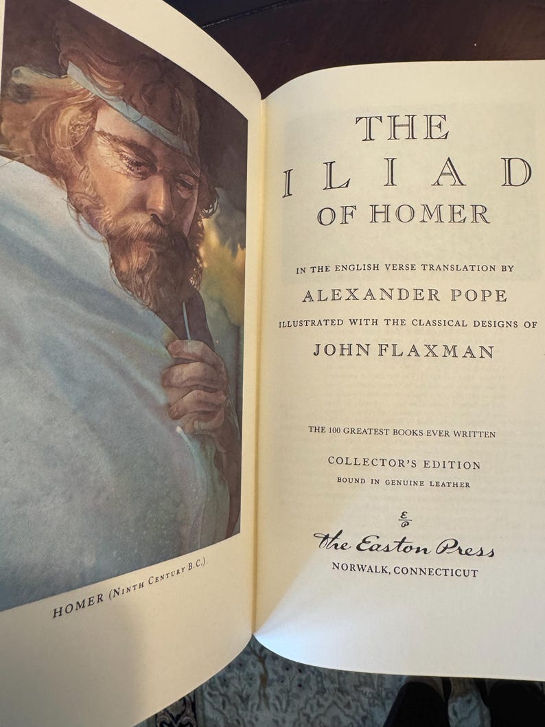 Może przedstawiać: Biały ceramiczny kubek z czarnym uchwytem i napisem "But First, Coffee" czarną, odręczną czcionką. Kubek stoi na białej powierzchni.