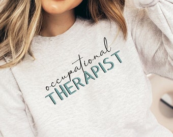 Könnte beinhalten: Ein graues Sweatshirt mit dem Text "occupational THERAPIST" in schwarzer und blaugrüner Schrift.