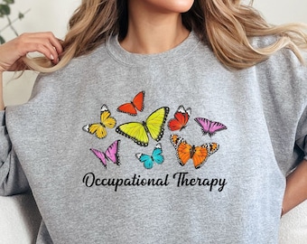 Op de afbeelding: Grijs sweatshirt met een kleurrijk vlinderontwerp en de tekst "Occupational Therapy".