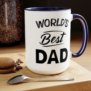 May include: White ceramic mug with a blue rim and handle. The mug has black text that reads "WORLD'S Best DAD".