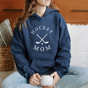 May include: A navy blue hoodie with a white graphic that says "Hockey Mom" with two crossed hockey sticks and a puck in the center.