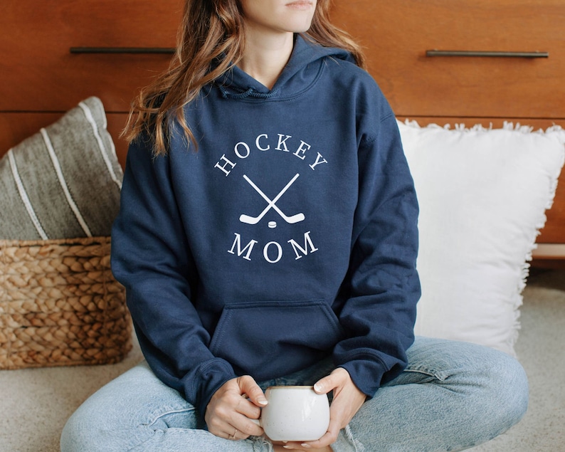 May include: A navy blue hoodie with a white graphic that says "Hockey Mom" with two crossed hockey sticks and a puck in the center.