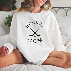 May include: White sweatshirt with the text "HOCKEY MOM" in black, along with crossed hockey sticks and a puck. The sweatshirt is a crew neck style.