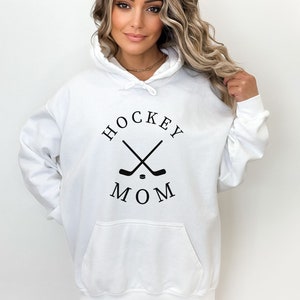 May include: White hoodie with a black graphic of crossed hockey sticks and a puck with the text "HOCKEY MOM" in a circle.