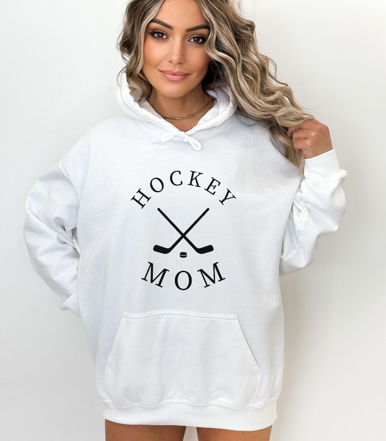 May include: White hoodie with a black graphic of crossed hockey sticks and a puck with the text "HOCKEY MOM" in a circle.