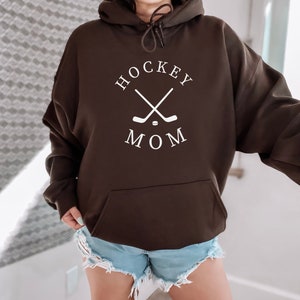 May include: A brown hoodie with a white graphic that says "HOCKEY MOM" with two crossed hockey sticks and a puck.