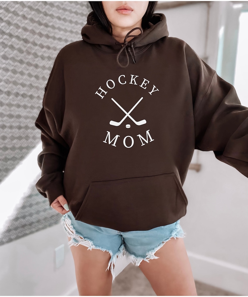 May include: A brown hoodie with a white graphic that says "HOCKEY MOM" with two crossed hockey sticks and a puck.