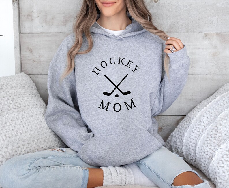 May include: Gray hooded sweatshirt with the text "HOCKEY MOM" in black lettering and a graphic of two crossed hockey sticks and a puck.