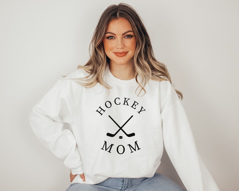 May include: White sweatshirt with the text "HOCKEY MOM" in black, along with crossed hockey sticks and a puck. The sweatshirt is a crew neck style.