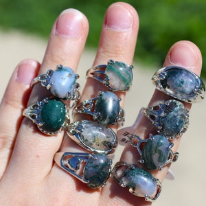 May include: A set of nine silver rings with green and white agate stones. The rings are stacked on a hand.