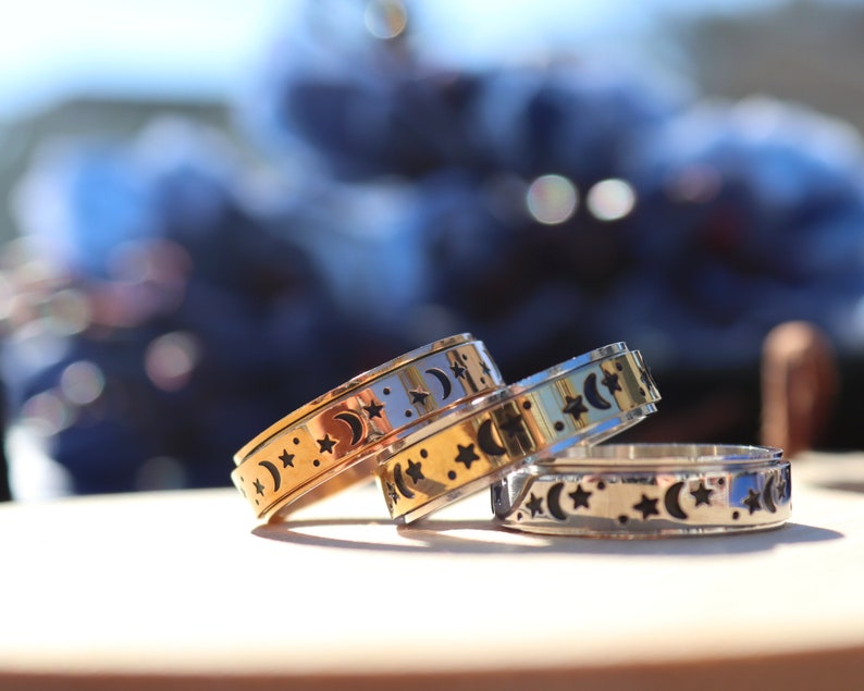 May include: Three gold and silver spinning rings with a moon and star design. The rings are stacked on top of each other.