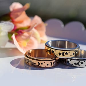 May include: Three spinning rings with a moon and star design. The rings are made of silver, gold, and rose gold.