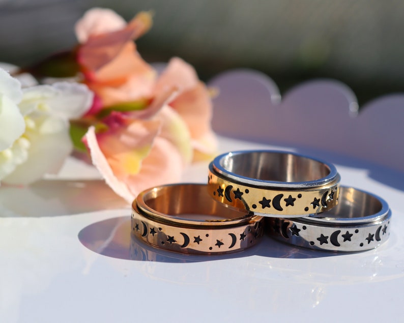 May include: Three spinning rings with a moon and star design. The rings are made of silver, gold, and rose gold.