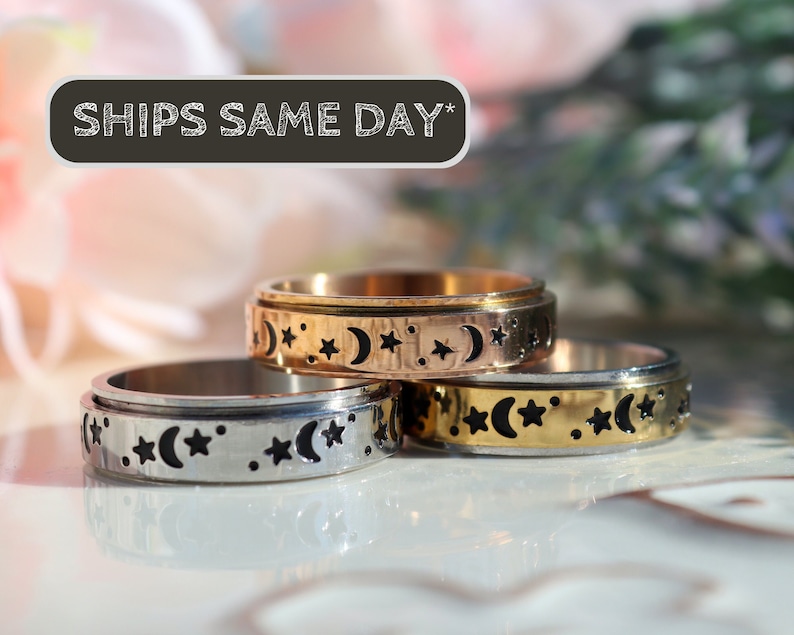 May include: Three spinner rings with a moon and star design. The top ring is gold, the middle ring is silver, and the bottom ring is silver. The rings are stacked on top of each other. The text 'SHIPS SAME DAY*' is visible in the background.