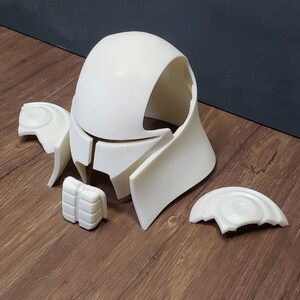 May include: Off-white, unassembled helmet parts. The components include a rounded top, side pieces, and smaller details. The pieces are arranged on a wooden surface, suggesting a DIY or cosplay project.