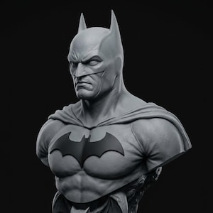 Puede incluir: Un busto gris de una figura de superhéroe con una capucha puntiaguda, una expresión facial severa y un prominente emblema de murciélago negro en el pecho. La escultura muestra una definición muscular detallada y una capa sobre los hombros.
