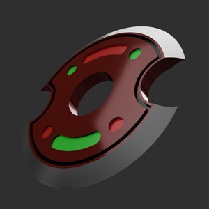 May include: A stylized, shield-shaped object with a dark red center and a silver edge. The center features green and red circular accents. The object has a glossy finish and is set against a dark gray background.