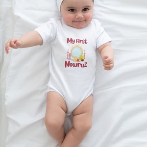 May include: A white baby onesie with a red graphic that says "My First Nowruz" and a colorful illustration of a Haft Seen table. The baby is wearing a white headband with a white bow.