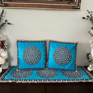 May include: Two blue throw pillows with intricate geometric patterns on a light blue background. The pillows are on a light blue table runner with a similar geometric pattern. The table runner has a brown fringe.