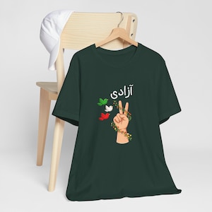 Unisex T-shirt featuring the Persian word “Azadi” meaning freedom, a hand making a peace sign wrapped in floral vines, and three doves in green, white, and red inspired by Iranian colors. Symbolic Iran freedom shirt representing peace, unity, and Woman Life Freedom movement.
