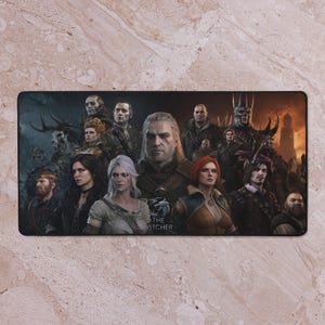 May include: Rectangular black desk mat featuring a group of characters from The Witcher series. The image includes Geralt of Rivia, Yennefer, Ciri, and other characters. The Witcher logo is visible at the bottom.