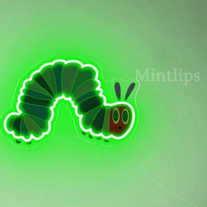 May include: Green neon light shaped like a caterpillar with a red face and two antennae. The light is mounted on a white wall in a room with a bookshelf and a toy car.