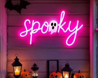 May include: A bright pink neon sign displaying the word spooky in a cursive script, with a white ghost silhouette replacing the letter o. The sign is mounted on a horizontal wood plank wall, accompanied by two black lanterns and three orange pumpkins.