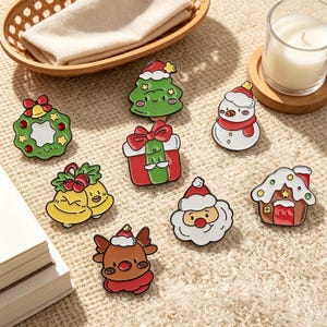 Pode incluir: Uma coleção de oito pins de esmalte com temas natalinos, incluindo uma guirlanda verde com um sino, uma árvore com gorro de Papai Noel, um boneco de neve, um presente, dois sinos amarelos, um rosto de Papai Noel, uma rena e uma casa de gengibre.