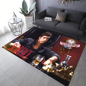 May include: A red and black area rug with a portrait of a man in a black shirt and a gold chain. The text "Scarface" and "World is Yours" is printed on the rug.