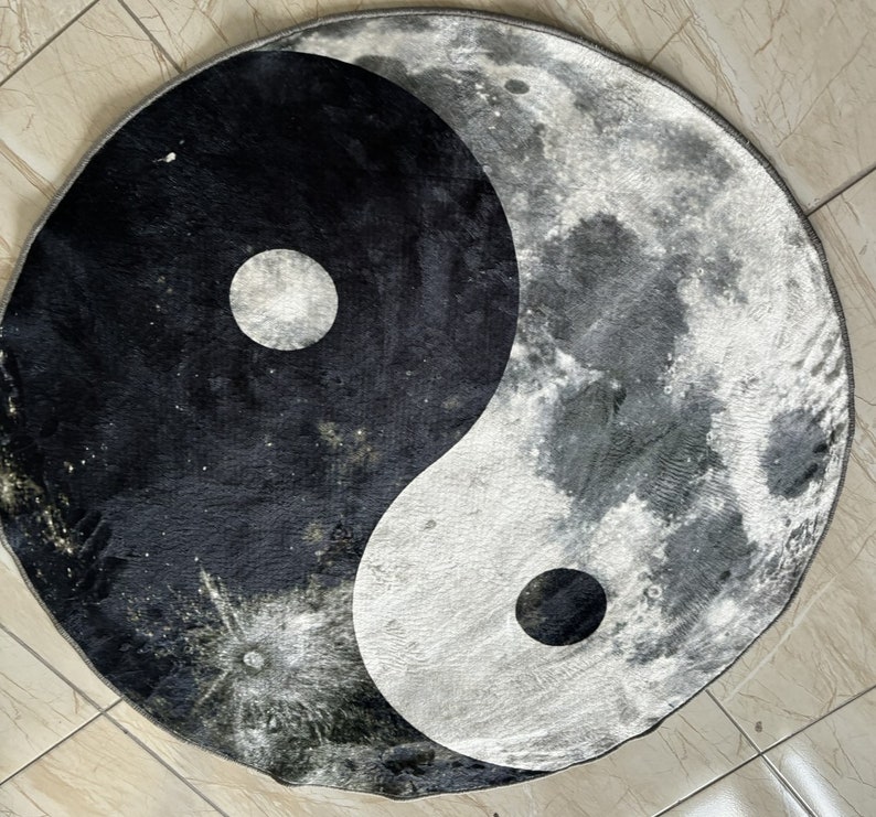 Może przedstawiać: Czarno-biały dywan yin yang z księżycowym wzorem po białej stronie. Dywan jest wykonany z miękkiego, pluszowego materiału i ma okrągły kształt.