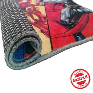 May include: A colorful rug with a superhero theme. The rug has a gray backing and a blue, red, and yellow design. The rug is rolled up and the edge is visible.