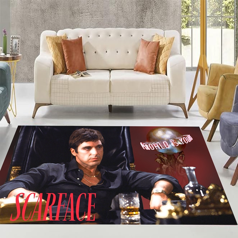 May include: A black and red rug with a picture of a man in a black shirt and a gold chain. The man is sitting in a chair with a glass of whiskey in his hand. The text "SCARFACE" is printed in red letters on the rug. The text "WORLD IS YOURS" is printed in white letters on a globe in the background.