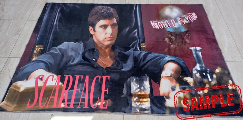 May include: A rug featuring a close-up image of Al Pacino as Tony Montana from the movie Scarface. The text "Scarface" is printed in red on the rug. The background is a red and black color scheme. The text "World is Yours" is printed in white on the rug.