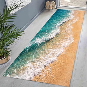 May include: A rectangular rug with a beach scene. The rug features a vibrant depiction of ocean waves in shades of turquoise and white washing onto a sandy beach in shades of tan and gold. The rug is placed on a light gray floor.
